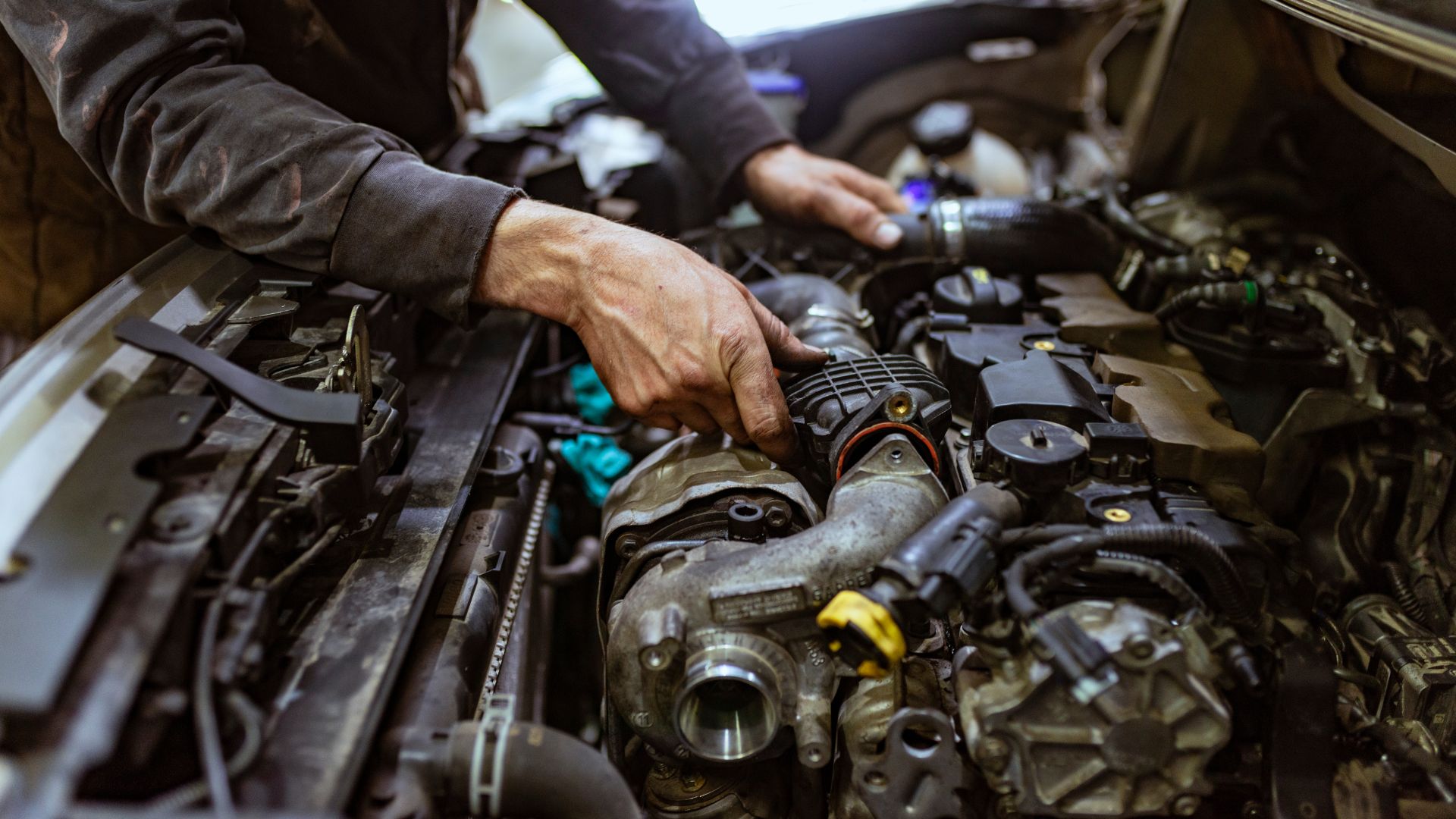 Mechanic's hand working on complex car engine with various metal components