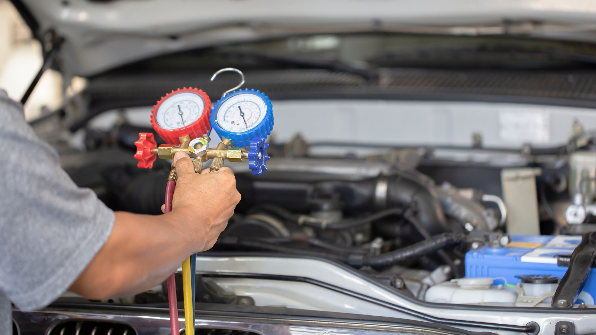 Mechanic using red and blue pressure gauges to check car's air conditioning