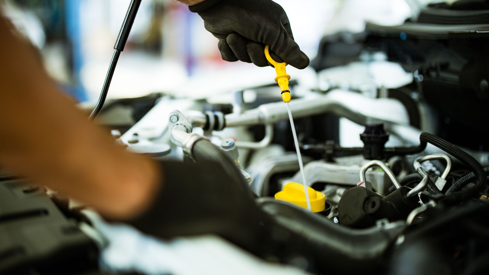 Mechanic checking engine oil level with yellow dipstick in car engine