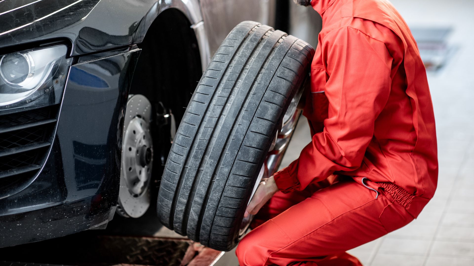Mechanic in red uniform changing tire on black car at auto service