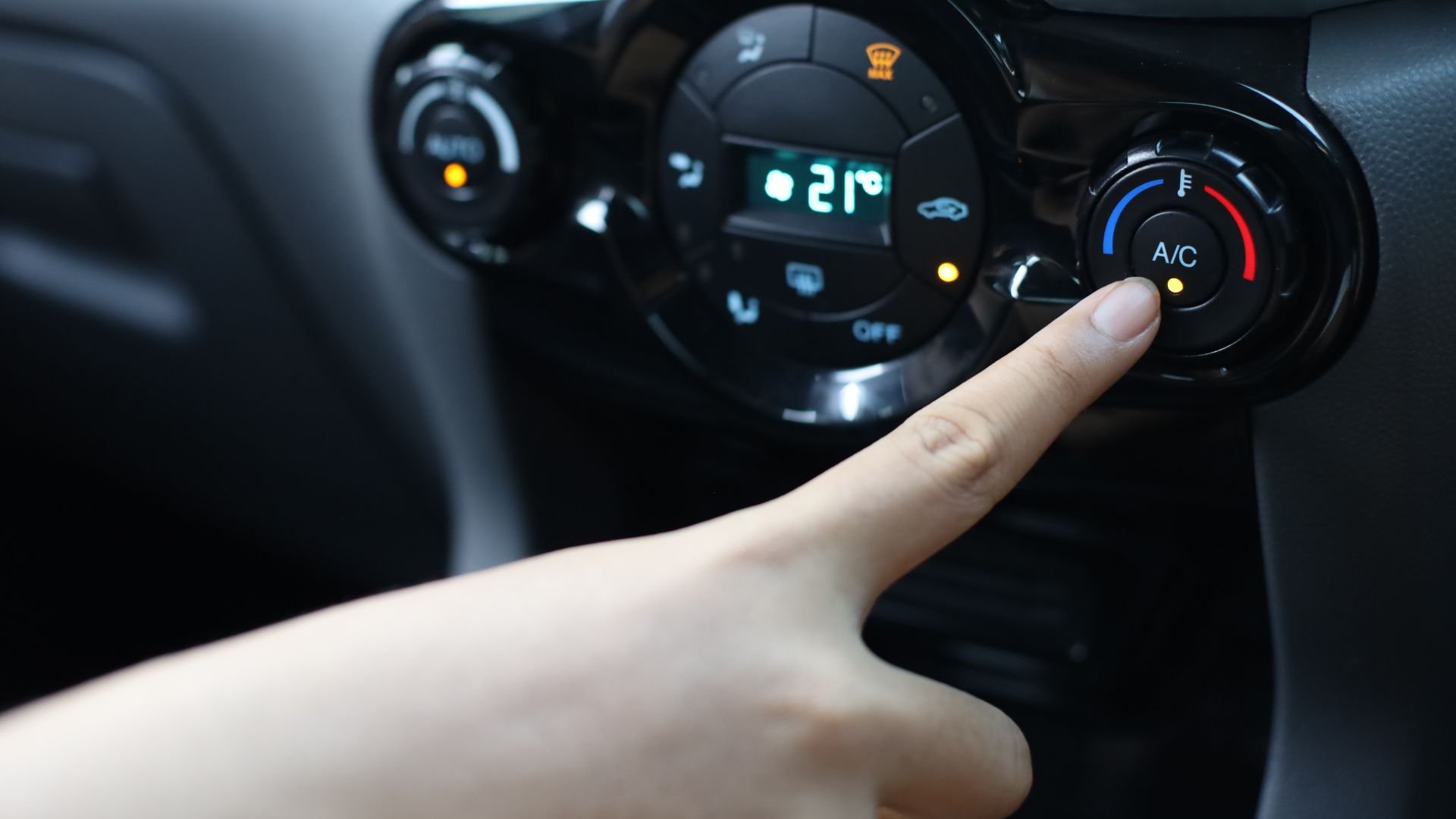 Finger adjusting car air conditioning control panel showing 21 degrees